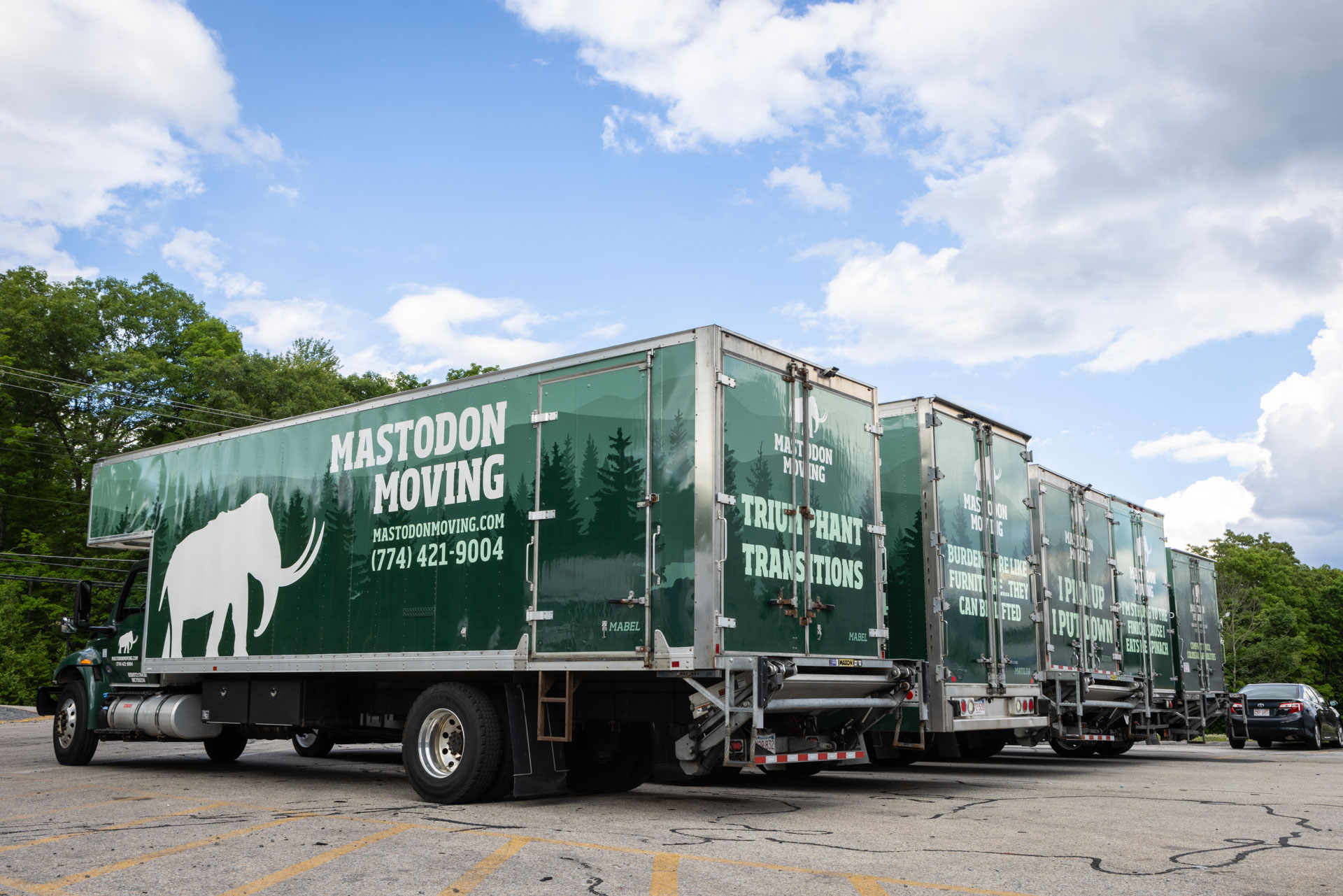Mastodon Moving's fleet of green box trucks lined up under a blue sky